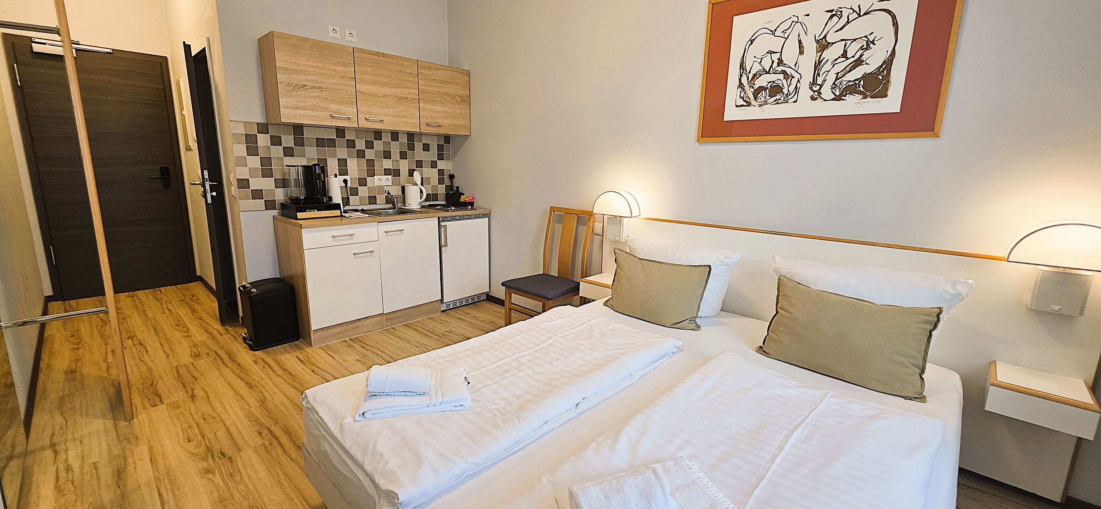 A hotel room with a bed, bedside table, lamp, and a kitchenette with a coffee maker and toaster.