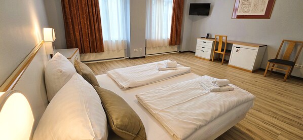 A hotel room with a bed, bedside tables, a desk, a chair, and a television.