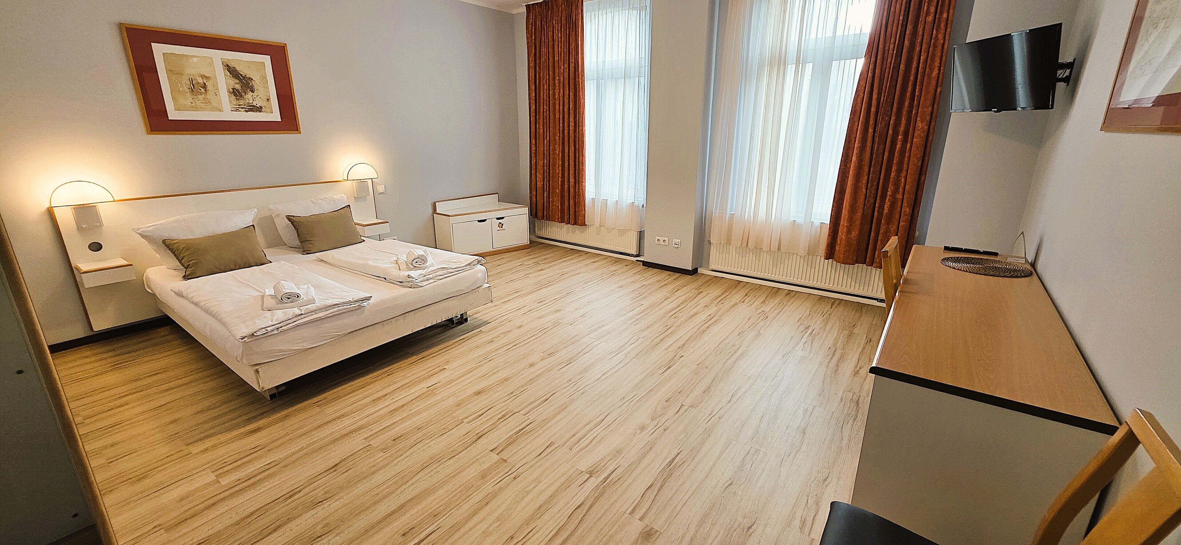 A hotel room with a bed, bedside tables, a TV, and a window with curtains.