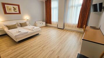 A hotel room with a bed, bedside tables, a TV, and a window with curtains.