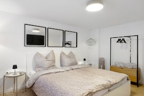 Une chambre à coucher comprenant un lit, des tables de chevet, un miroir, un luminaire suspendu et une armoire.
