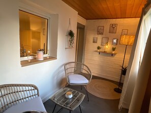 Une pièce chaleureuse avec des fauteuils en osier, une petite table, une fenêtre donnant sur un beau paysage, une étagère avec des plantes et un lampadaire.