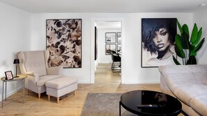 Un salon moderne avec un canapé, un fauteuil et une table basse. Deux grandes peintures abstraites ornent les murs.