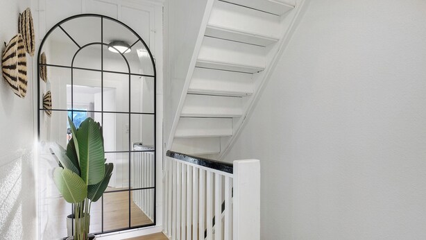 Un couloir avec une rambarde blanche, une plante en pot et un mur miroitant.