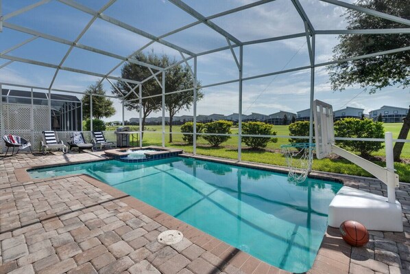 A covered outdoor swimming pool with lounge chairs, a hot tub, and a basketball hoop. - Magic & Muggles: Private Pool/Spa, BBQ, Game Room! (Kissimmee)