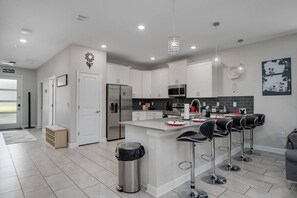 A modern kitchen with white cabinetry, stainless steel appliances, and a central island with bar stools. - Magic & Muggles: Private Pool/Spa, BBQ, Game Room! (Kissimmee)