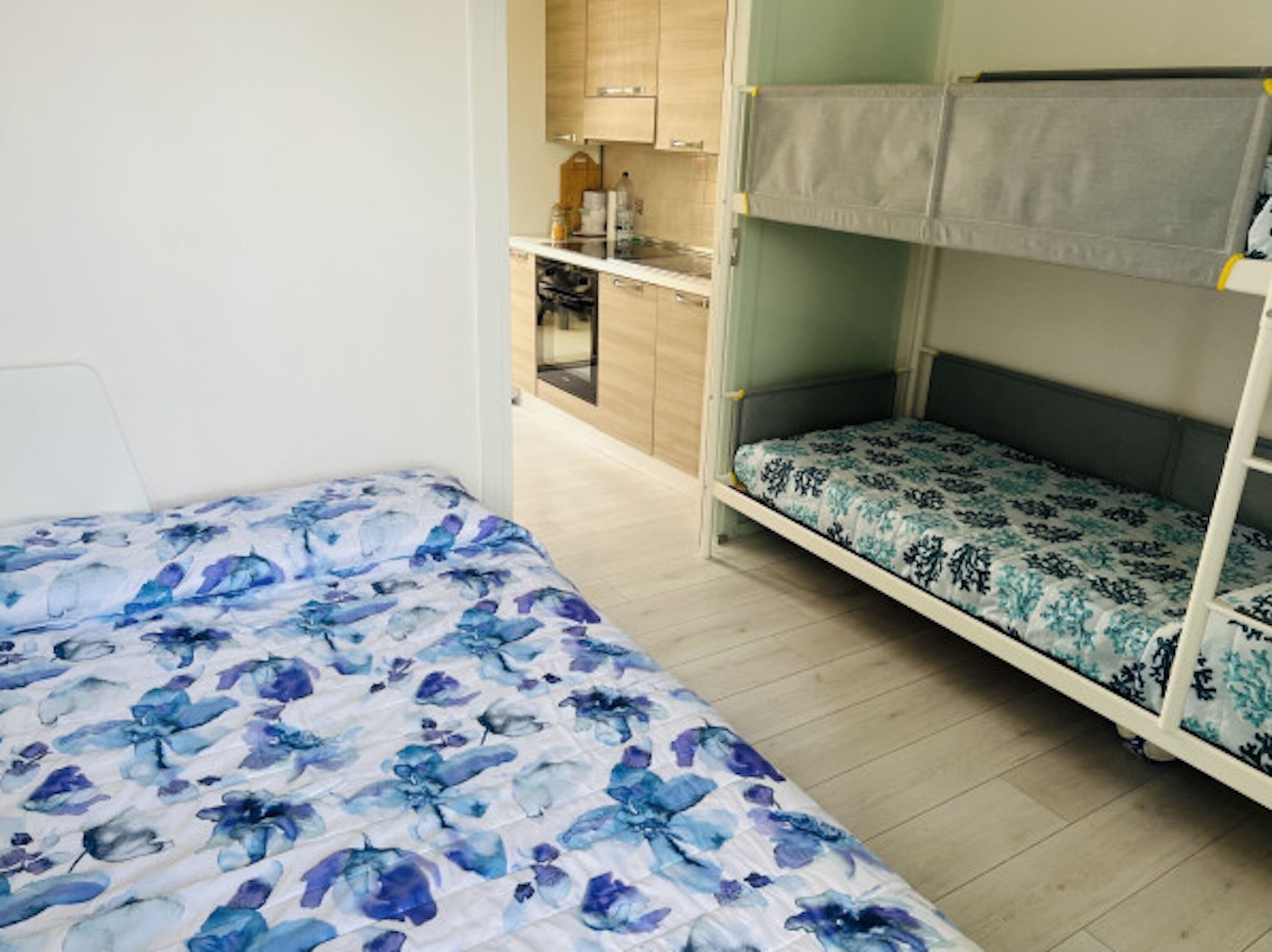 A bunk bed with floral bedding, a kitchenette with wooden cabinets, and a small bathroom.