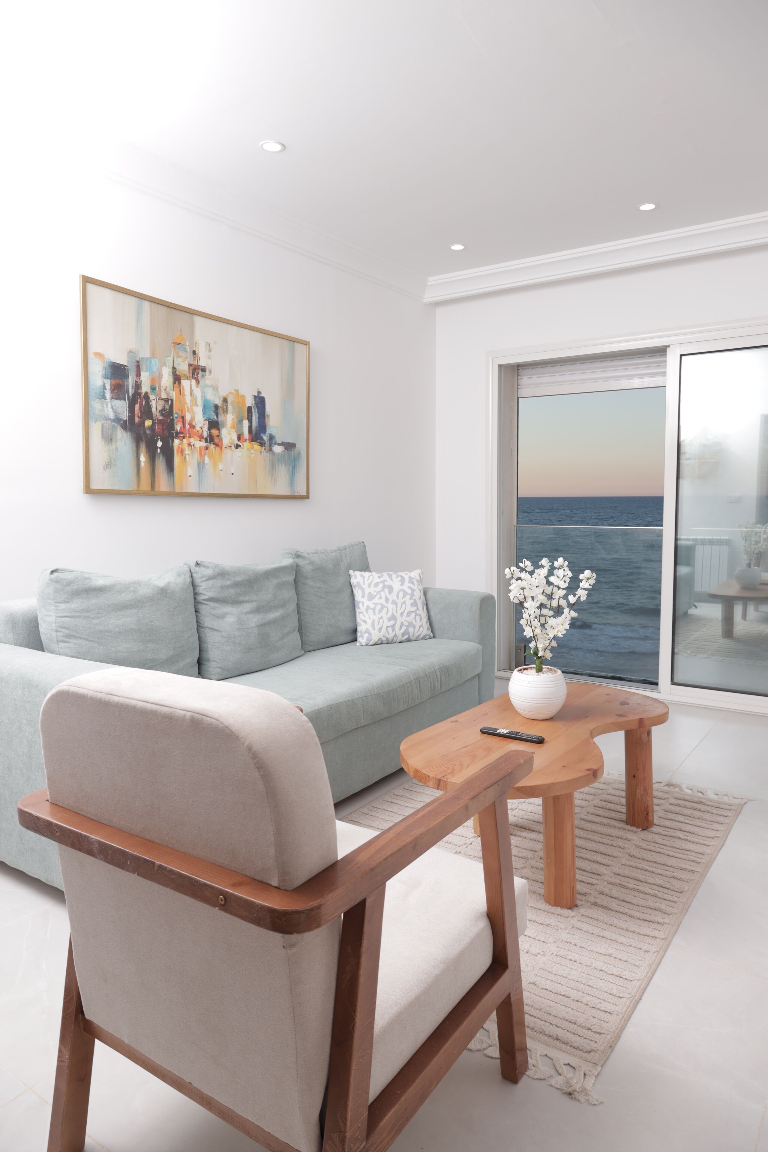 A modern living room with a light blue sofa, a wooden coffee table, and a painting on the wall.