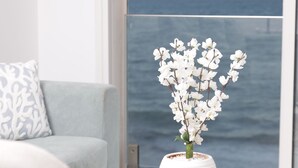 A room with a wooden coffee table, a white vase with white flowers, a remote control, and a view of the ocean through large windows. - L'écume Blanche - Apartment With Feet in the Water (La Marsa)
