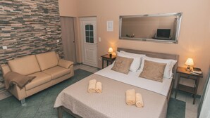 A hotel room with a bed, a sofa, a stone wall, a door, a mirror, and two bedside tables with lamps. - Villa Chiara Opatija Apartment Rustica (Ičići)