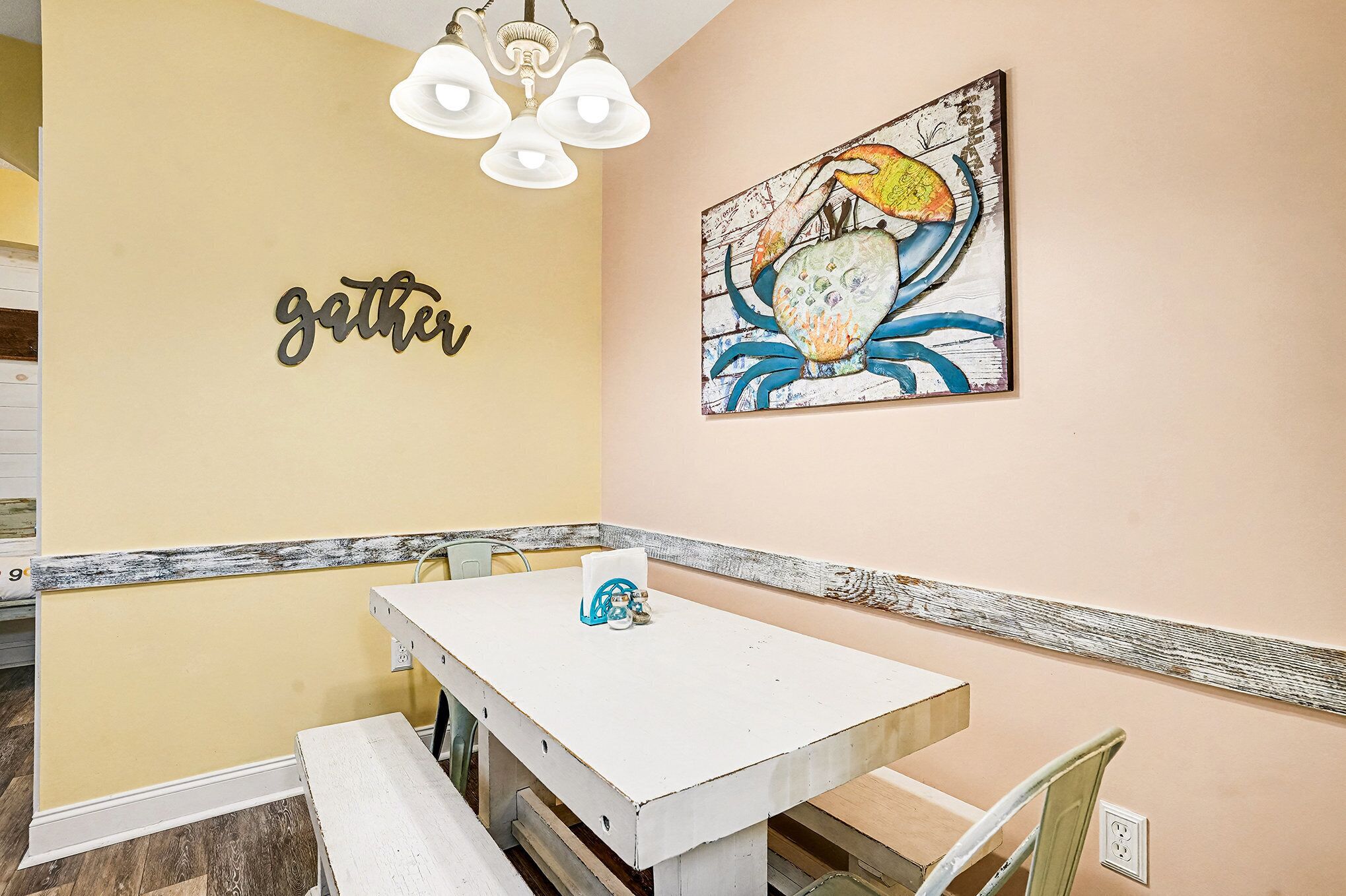 A dining area with a white table, chairs, and a 'gather' sign on the wall.