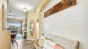Een gang met een houten bankje, een surfplank en een kapstok aan de muur.