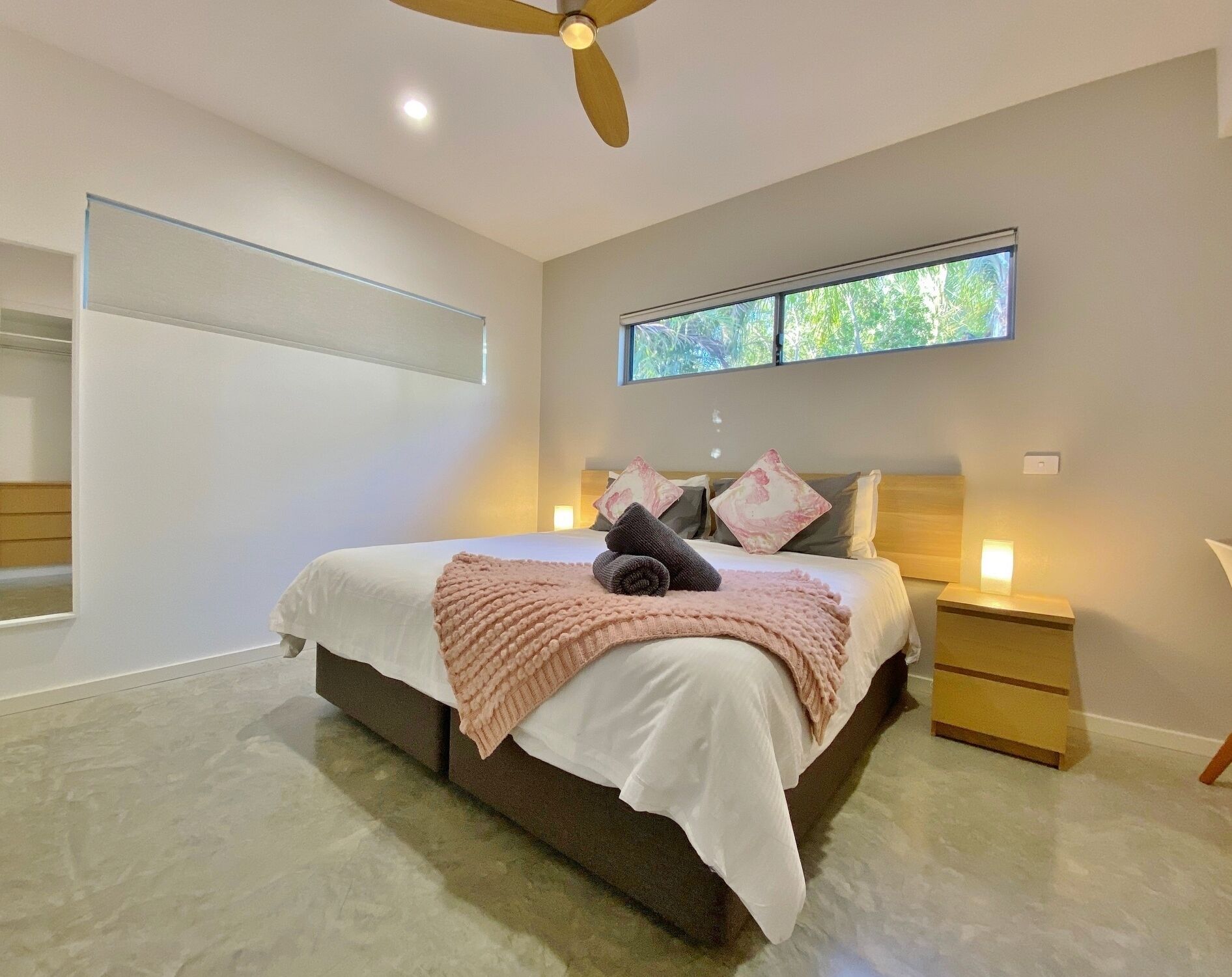 Une chambre moderne avec un grand lit, un ventilateur de plafond, une fenêtre donnant sur un paysage verdoyant et des lampes de chevet.
