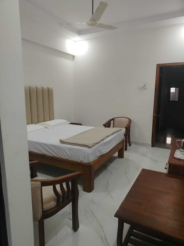 Un dormitorio con cama, dos sillas, una mesa, un ventilador de techo y una puerta.