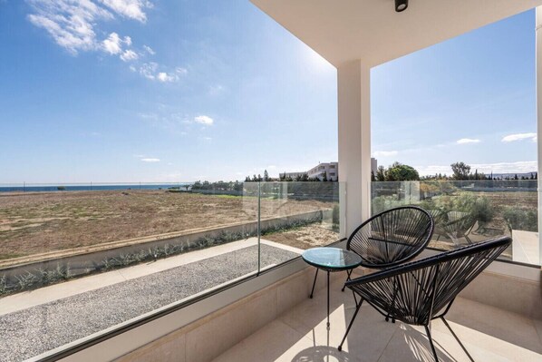 A balcony with a glass railing overlooking a beach and a clear sky.