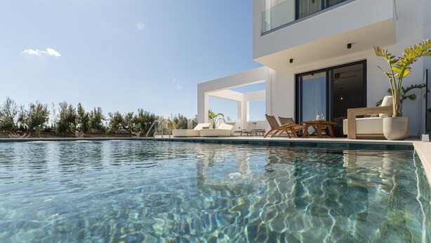 Un espace piscine moderne avec une eau cristalline, des chaises longues et un bâtiment doté de grandes fenêtres et d’un balcon.