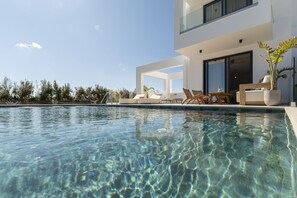 A modern pool area with clear water, lounge chairs, and a building with large windows and a balcony.