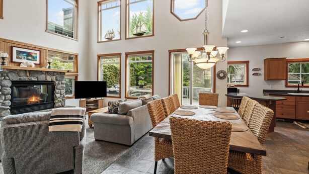 Un salón espacioso con chimenea, ventanas amplias, una zona de comedor con sillas de mimbre y una cocina con armarios de madera.