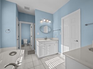 A bathroom with a white bathtub, a sink with a mirror above, and a toilet. - Soundfront Living with Ocean Views, Private Dock & Pool (Emerald Isle)