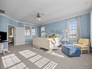 A bedroom with a bed, a chair, a desk with a TV, and two windows with blinds. - Soundfront Living with Ocean Views, Private Dock & Pool (Emerald Isle)