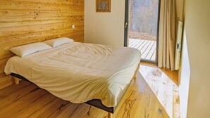 Een slaapkamer met een houten hoofdeinde, een bed met wit beddengoed, een houten vloer en uitzicht door een glazen deur.