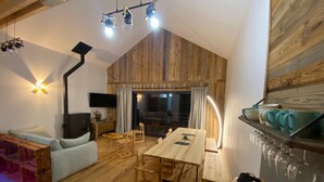 Een gezellige woonkamer met houten vloer, een eettafel en een bank. Een televisie is aan de muur bevestigd en er is een raam met gordijnen.