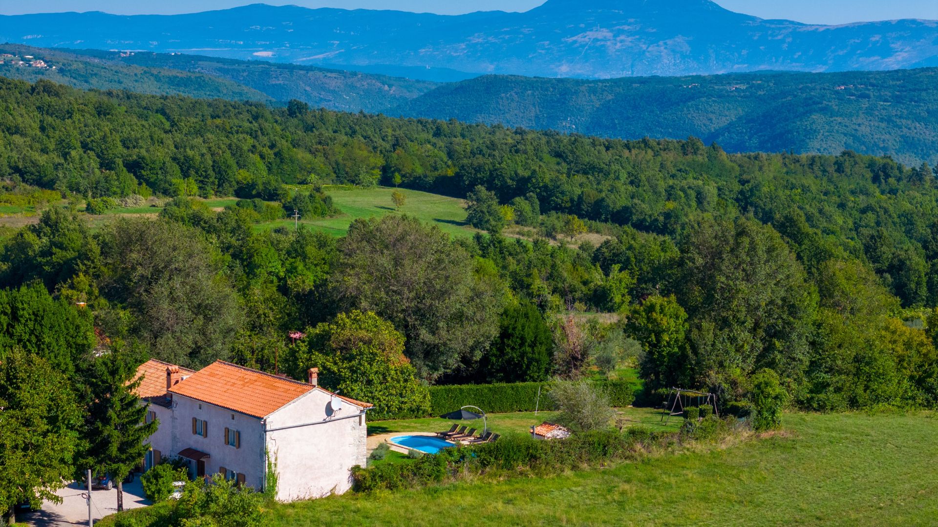 A white villa with a red-tiled roof, a swimming pool, and a garden.