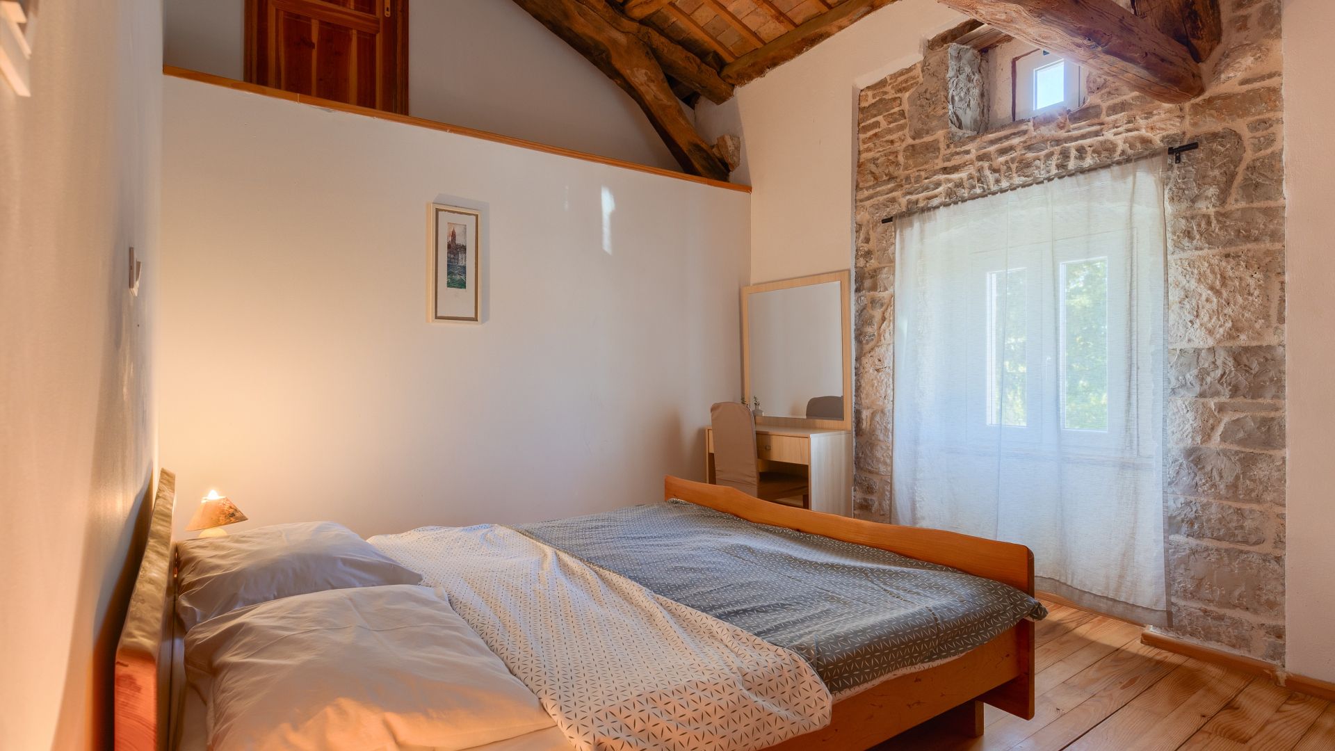 A bedroom with a wooden bed, a desk, and a stone wall.