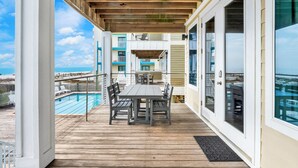 A covered outdoor deck with a pool, a table and chairs, and a view of the ocean. - Gulf-Front Duplex | Pet Friendly | Shared Pool (Gulf Shores)