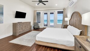 A bedroom with a bed, a TV, a ceiling fan, an air conditioner, a wooden dresser, a chair, and a view of the ocean through a sliding door. - Gulf-Front Duplex | Pet Friendly | Shared Pool (Gulf Shores)