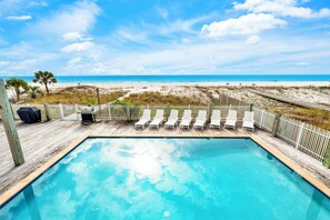 A swimming pool with a wooden deck, white lounge chairs, and a view of the beach and ocean. - Gulf-Front Duplex | Pet Friendly | Shared Pool (Gulf Shores)