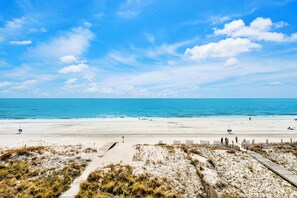 A beach with a clear sky, sandy shore, and a wooden boardwalk leading to the water. - Gulf-Front Duplex | Pet Friendly | Shared Pool (Gulf Shores)