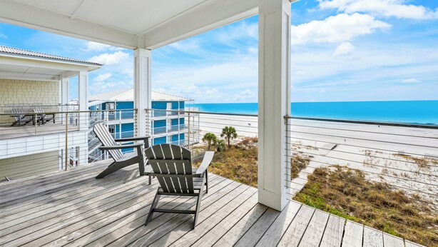 Una terraza de madera con una silla y vistas a la playa y al océano.