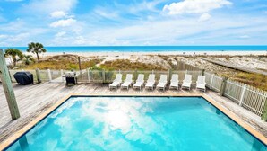 Una piscina con muelle de madera, sillones de descanso blancos y vista a la playa y el océano.