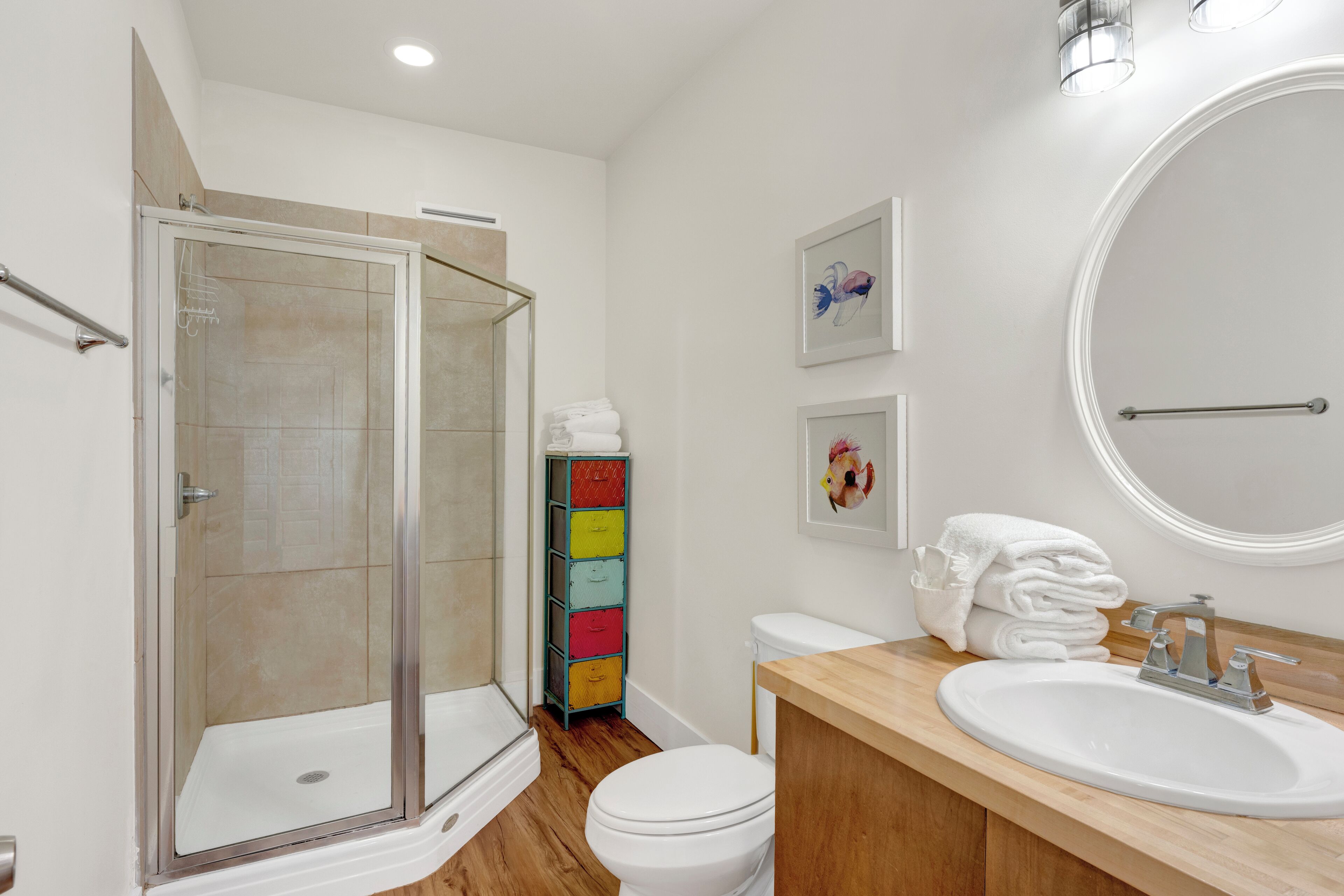 Un baño moderno con cabina de ducha de vidrio, tocador de madera, inodoro blanco y un mueble de almacenaje de colores.