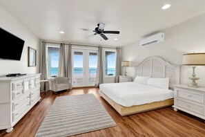 A bedroom with a bed, a TV, a ceiling fan, an air conditioner, a nightstand, a lamp, a chair, and a view of the ocean through large windows. - Gulf-Front Oasis | Pet Friendly | Private Pool (Gulf Shores)