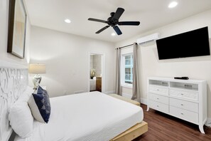 Una camera da letto con un letto, una ventola a soffitto, una TV, un comò e una finestra con tende.