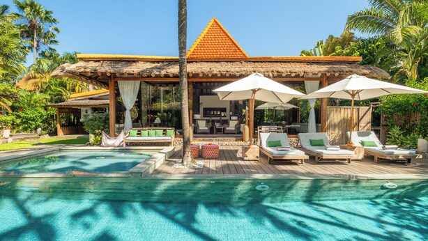 A poolside area with lounge chairs and umbrellas, a thatched-roof structure, and a clear pool. - Private luxury 2 bedroom villa in the heart of Berawa! (Canggu)