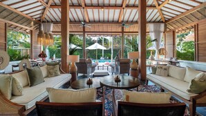 A spacious outdoor lounge area with wooden furniture, a central table, and a view of a swimming pool. - Private luxury 2 bedroom villa in the heart of Berawa! (Canggu)