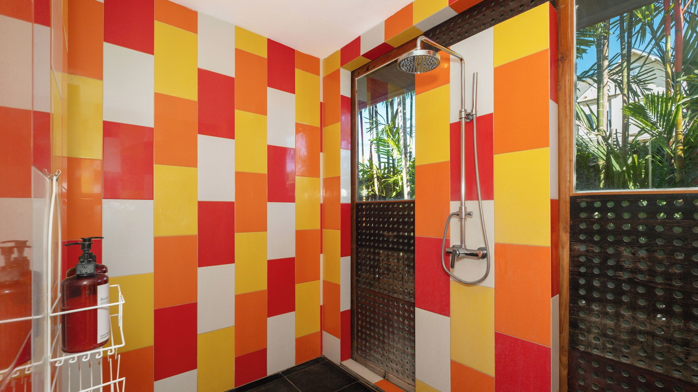 Une salle de bain avec un carrelage à motifs à carreaux, une douche dotée d’une porte en verre et un flacon de gel douche posé sur une étagère.