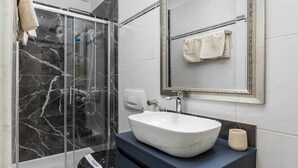 Un baño moderno con ducha de vidrio, un lavabo blanco y un espejo grande.