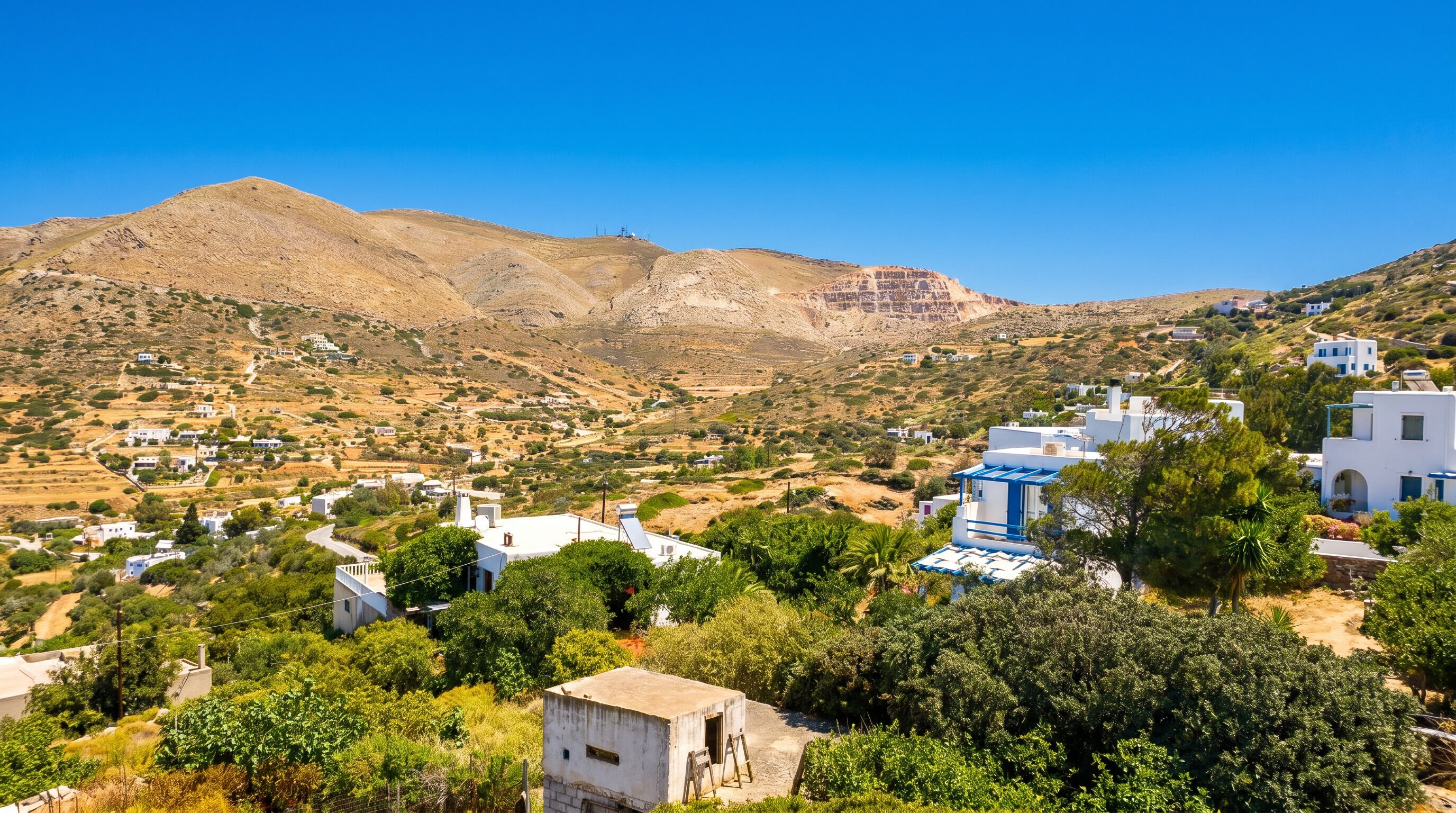 A coastal village with white buildings, a mountain in the background, and lush greenery.