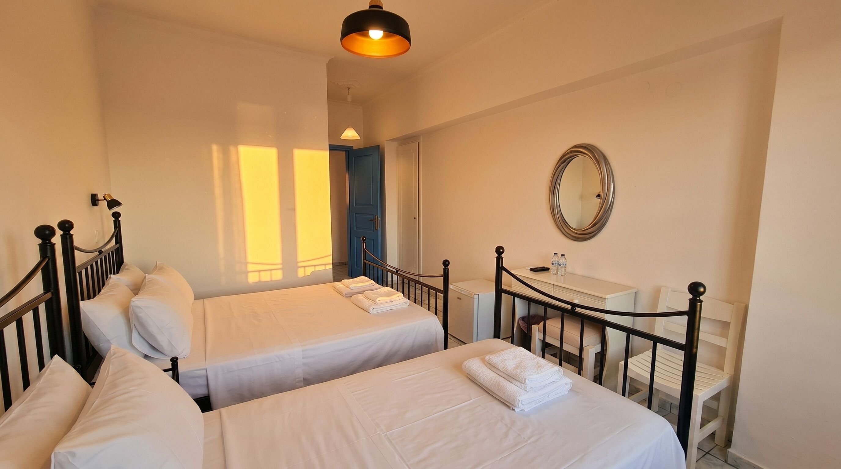 A hotel room with two beds, a desk, a mirror, and a wardrobe.