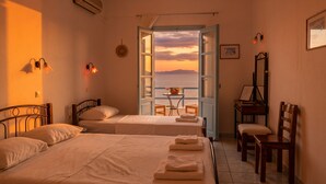 A hotel room with two beds, a desk, a chair, and a view of the sea. - Lume D'oro Syros (Kini)