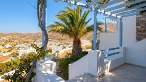 A white building with a stone wall, a palm tree, and a view of a town. - Lume D'oro Syros (Kini)