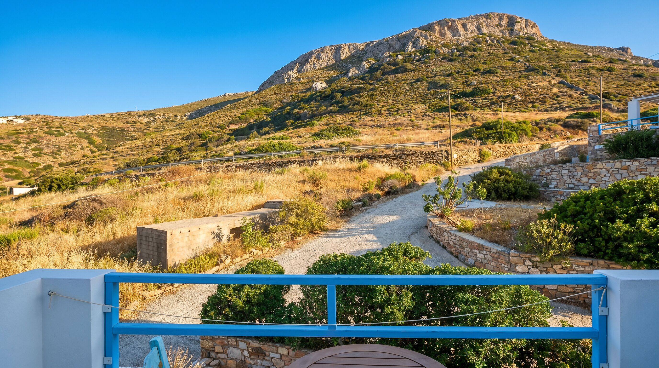 A mountainous landscape with a dirt path leading to a stone wall and a blue railing.