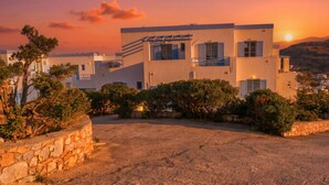 A modern building with a flat roof, multiple windows, and a stone wall in the foreground. - Lume D'oro Syros (Kini)