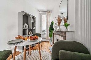 A modern living room with a dining table, chairs, a grey bookshelf, and a fireplace. - Close to Paris City Center | Eiffel Tower View (Paris)