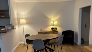 Een eetgedeelte met een ronde houten tafel, vier stoelen, een vloerlamp en een bijzettafeltje met een lamp.