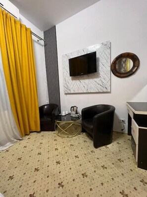 Une pièce avec un téléviseur fixé au mur, qui est recouvert de marbre, un miroir rond, un fauteuil en cuir noir, une petite table basse et un tapis à motifs.